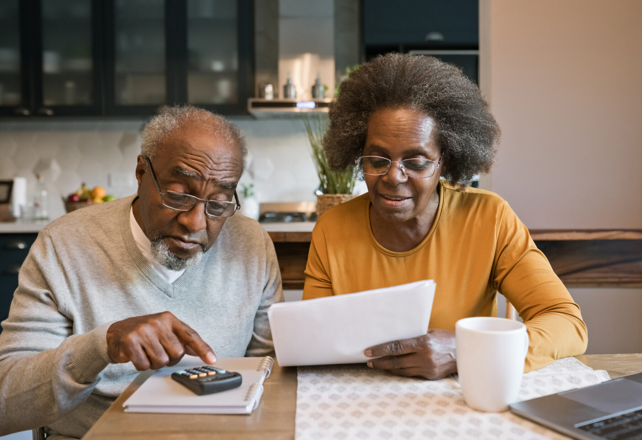 Senior woman and man sitting at the table at home and going through bills. Elderly lady holding documents in hands. They are planning budget.